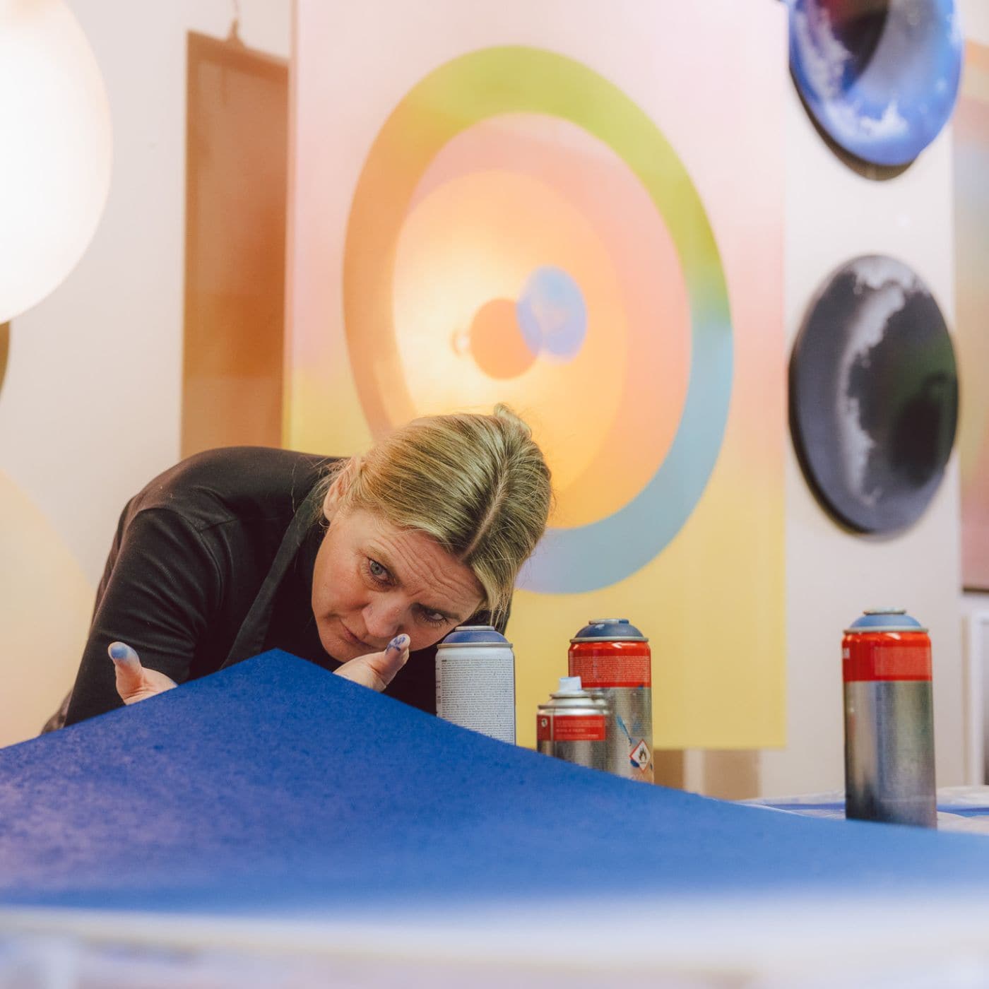 Artist working with blue surface surrounded by spray cans, creating layered acoustic graffiti art in vibrant circular forms.