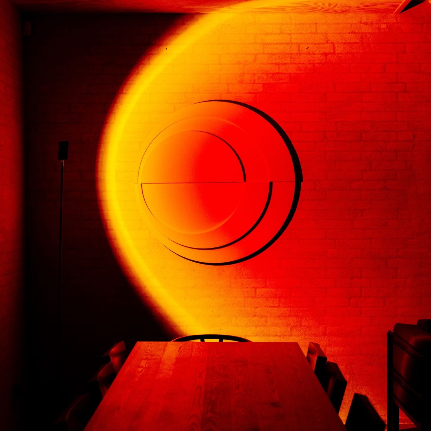 Light art for walls with red and yellow gradients illuminating acoustic panels in a modern dining room setting.