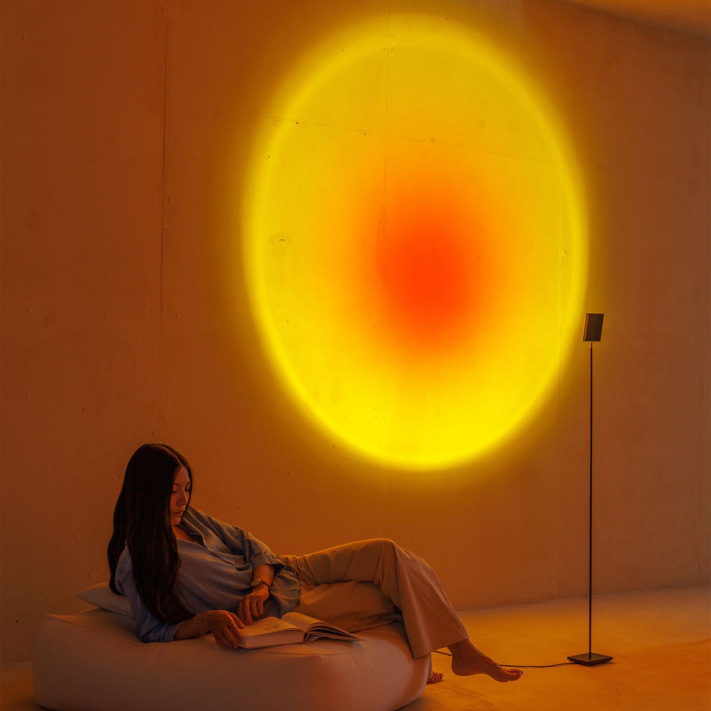 Light art for walls casting a soft yellow and red halo while a woman reads in a calm, minimalist interior setting.