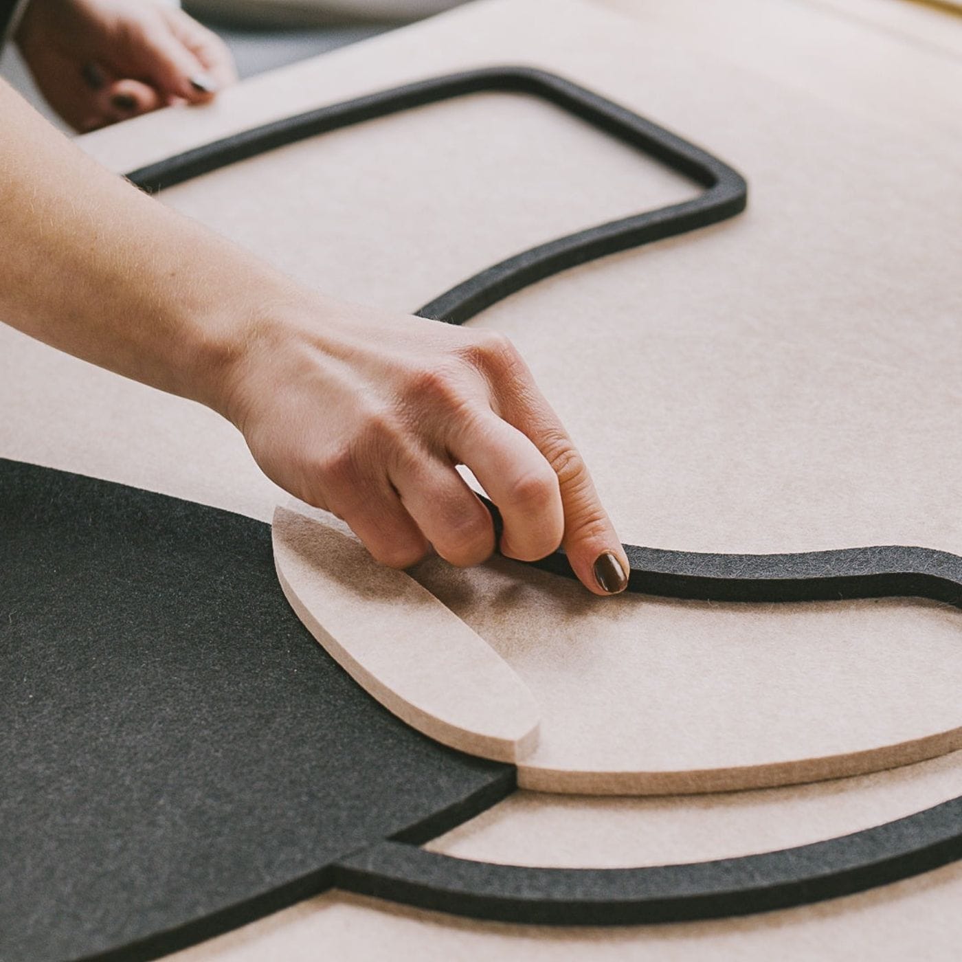Close-up of hands assembling layered acoustic panels in a clean, organic design, showcasing minimalist art in progress.