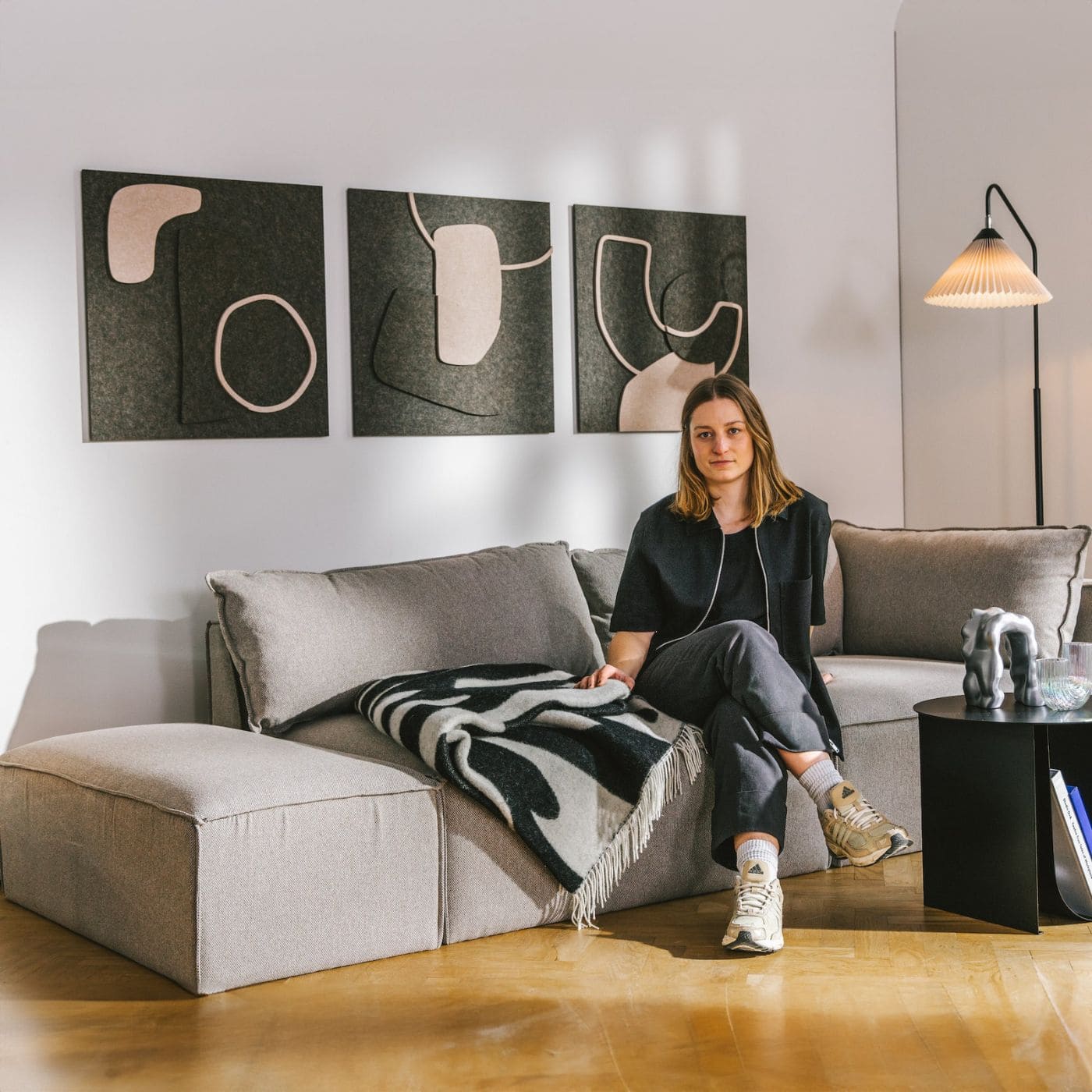 Woman seated in modern living room with three-panel nordic bauhaus art featuring soft abstract acoustic forms on the wall.